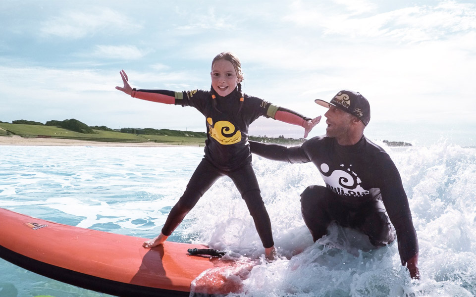 surfer teaching a young girl how to surf